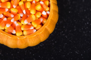 Ceramic pumpkin bowl filled with Halloween candy corn. Top view with dark background and copy...