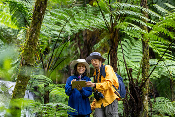 Team of the Asian naturalist looking at map while exploring in the tree fern forest for surveying and discovering the rare biodiversity species and ecologist on the field study usage