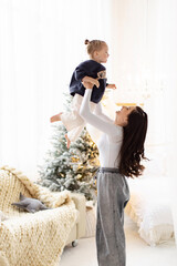 A mother joyfully lifts her child in the air, creating a heartwarming moment indoors. A Christmas...