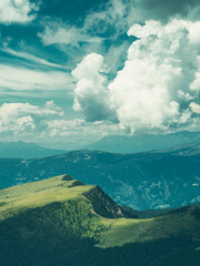 Sunlit mountain slopes in the Dolomites, Italy. Vibrant green meadows and forested hills bathed in golden light beneath dramatic summer clouds — a breathtaking view of alpine beauty.