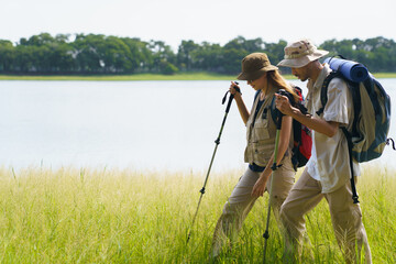 Couple hiking near lake in grassy meadow, enjoying scenic nature view.