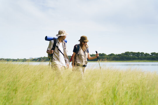 Couple hiking near lake in grassy meadow, enjoying scenic nature view. - Powered by Adobe