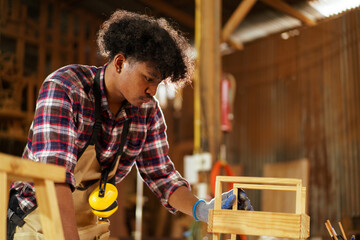 Black carpenter inspects finished wood in factory for quality control.