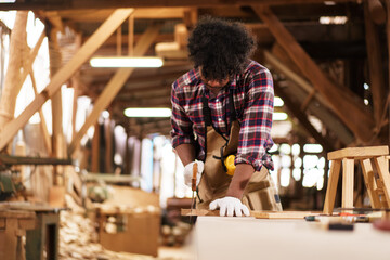 African American carpenter sawing wood with hand saw in sawmill factory
