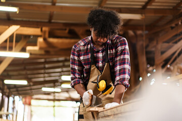 African American carpenter sawing wood with hand saw in sawmill factory