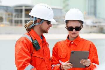 Male and female engineers discussing data on tablet at oil refinery.