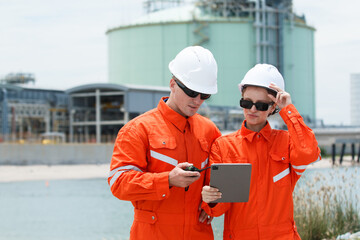 Male and female engineers discussing data on tablet at oil refinery.