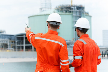 Refinery engineers discussing data on digital tablet at oil plant.