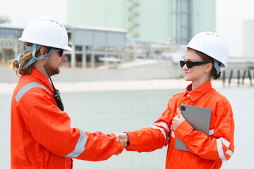 Male and female engineers shaking hands at oil refinery facility.