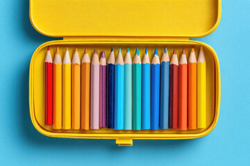 Yellow pencil case with colored pencils on blue background. Back to school. Flat lay, top view, copy space
