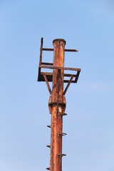 Close-up of an old rusty metal pole structure against clear blue sky. Industrial decay, weathered steel, and minimal composition showing texture, corrosion, and aging over time in outdoor environment