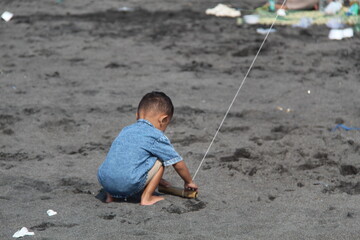 Young boy flying a kite while squatting on a dark sandy beach. Ideal for childhood, outdoor, beach, or recreational-themed visual content
