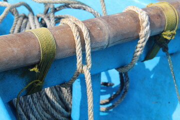 Close-up of ropes tied to a wooden pole on a blue fishing boat. Detail of marine knots and textures used in traditional fishing vessels under bright sunlight