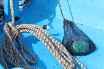 Close-up of a thick marine rope and a small fishing net on a blue boat deck under sunlight. Detail of nautical equipment used by fishermen on a traditional wooden boat.