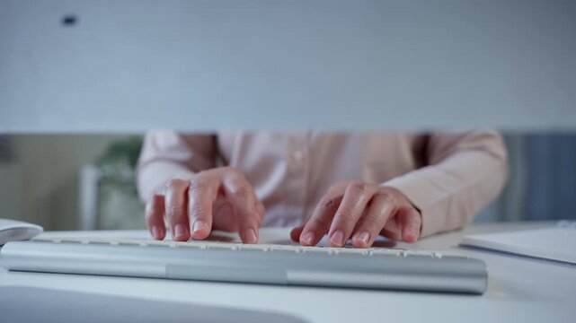 Female professional typing quickly on wireless keyboard, showcasing efficient data entry skills in bright, modern office workspace with clean white desk