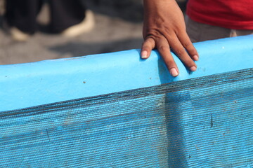 A hand resting on the turquoise edge of a netted container. Ideal for manual labor, fishing, market, or texture-themed visual content