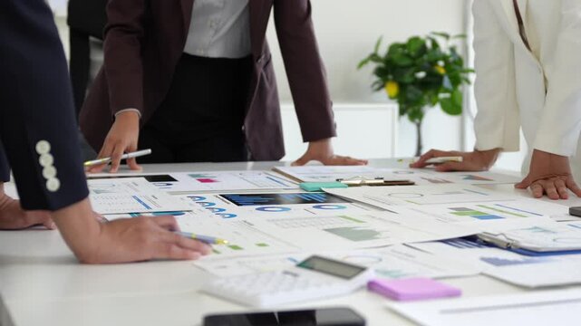 Business team analyzing marketing data and financial charts spread out on a table, pointing and discussing strategies for growth and success