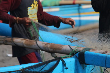 Fishermen preparing fishing nets on the beach, repairing and untangling mesh before going to sea. Daily coastal activity showing hard work, teamwork, and traditional fishing culture in a seaside villa