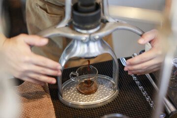 Focused barista making espresso with manual coffee press machine. Aromatic hot coffee drink drips into glass cup for morning caffeine beverage in modern cafe