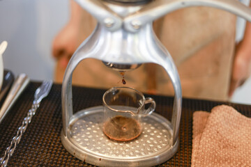 Focused barista using manual espresso press to extract fresh, aromatic coffee. dark liquid drips into small glass cup, perfect morning brew ritual in cafe