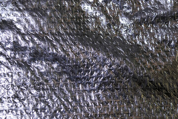 Shiny silver metallic foil background with crumpled rough surface. This abstract texture features modern industrial material with unique pattern and reflective quality