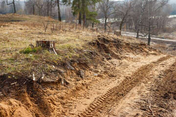 Gritty dirt track with distinct tire marks ascends a bare, erosion-prone slope. Scattered tree stumps hint at deforestation, beneath a dull, late autumn sky