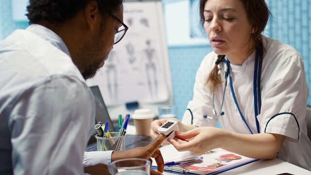 Physician measuring the oxygen saturation and pulse rate using an oximeter during check up visit, consulting her patient with modern medical equipment. Vital signs measurement. Camera B.