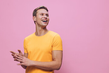 Cheerful smiling young man with light skin wearing a bright yellow t-shirt, standing against a pink...