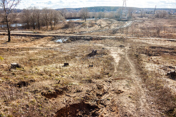 Gnarly dirt paths cut across a raw, parched expanse dotted with old tree stumps and withered scrub. A river and distant woods frame the untamed scene