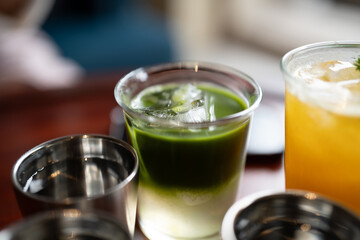 Refreshing green drink in glass with ice, surrounded by metallic cups.