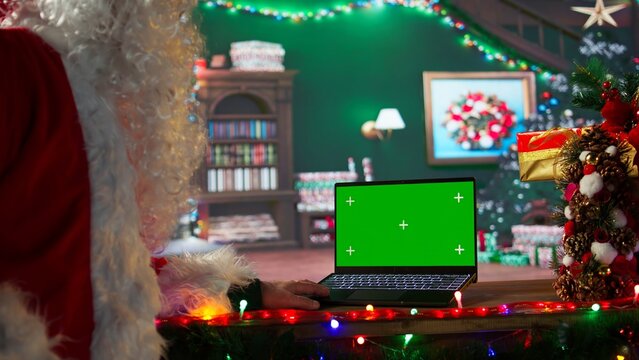 Santa Claus sitting next to copy space screen on device and reading letters from children around the world. Old man Saint Nicholas spreading his festive cheer for the holiday period. Camera B.