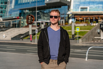 Handsome young man in black glasses stands in front of skyscrapers in Moscow City.