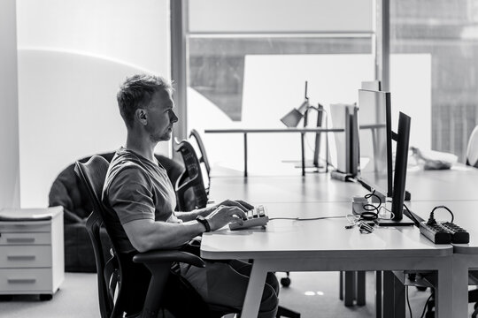 A young man, a manager or an IT specialist, sits at his workplace at a computer. Black and white photo