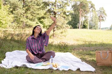 happy, smiling 40-year-old woman takes a selfie in a park. A cheerful, attractive woman relaxes outdoors. Social media concept.
