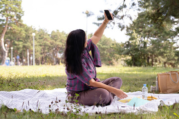 happy, smiling 40-year-old woman takes a selfie in a park. A cheerful, attractive woman relaxes outdoors. Social media concept.
