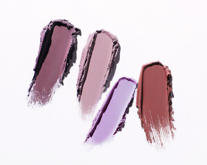 Four vertical eyeshadow swatches with pigment on white background. Close-up of loose cosmetics texture, natural dark pink or plum colors, pearlescent effect. Professional studio light