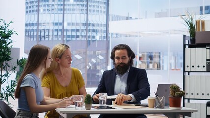 Financial advisor talks with clients about importance of budgeting in income management, offering them written guide. Mom and daughter explore best practices for building money saving habits, camera B