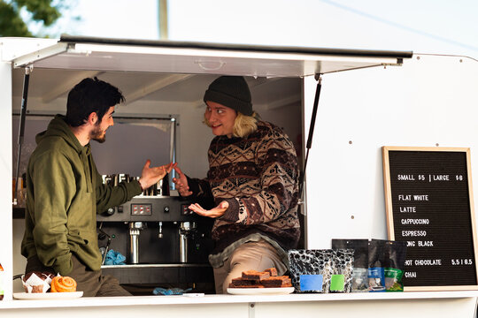 Young coffee maker chatting with trainee barista in coffee van shop