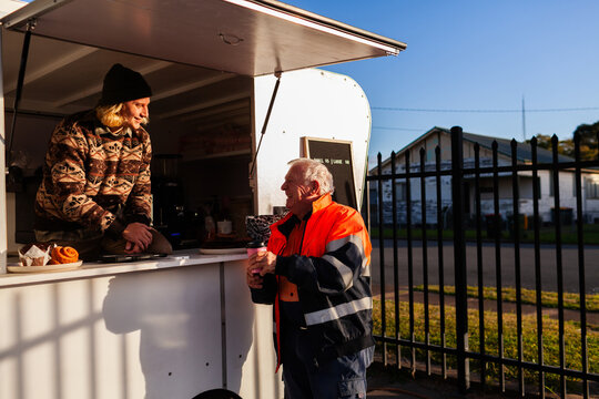 happy older Aussie workman in high vis workwear buying warm takeaway coffee from van