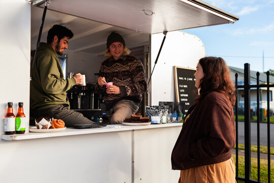 Young woman buying morning latte from small business coffee van chatting with baristas