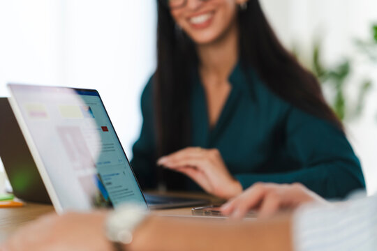 Two colleagues collaborate on a project, using laptops and a mobile device in a bright office setting.