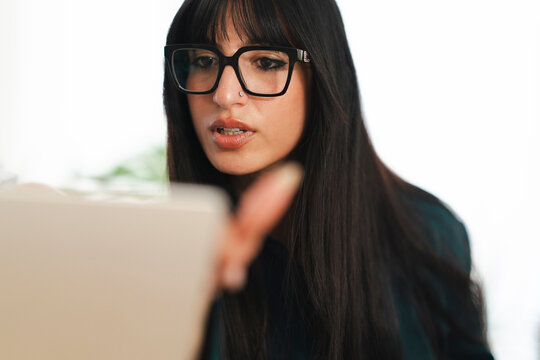 A young woman wearing glasses leans forward, her hand reaching out towards a blurred object, suggesting focus and engagement with her task.