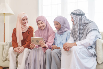 portrait of happy muslim family in traditional clothes sitting on sofa in living room at home,enjoying tablet together,family holiday leisure time