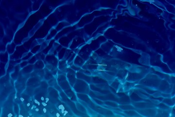 Blue water with ripples on the surface. Defocus blurred transparent blue colored clear calm water surface texture with splashes and bubbles. Water waves with shining pattern texture background.