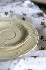Two elegant vintage plates with embossed patterns placed on a white fabric with golden stars, creating a soft and cozy still life composition.