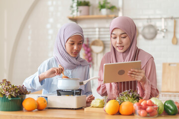 muslim girl and mother in hijab prepare organic vegetables and fruits, together with learning on digital tablet while cooking food in the kitchen