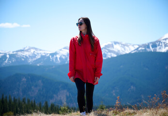 Hiker girl on background of snowy mountains. Young female in red sport jacket and sunglasses hiking in the mountains. Incredible landscape reflects peace and freedom.