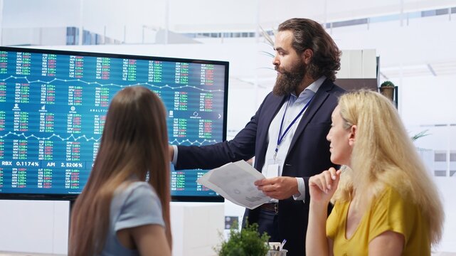 Team leader in company financial department showing stock portfolio on big screen containing collection of investment assets. Businessman showing stock demand surge in large display, camera B