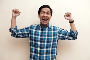 Fototapeta premium Southeast Asian man wearing flannel shirt showing happy excited expression with clenched fist, on white isolated background.