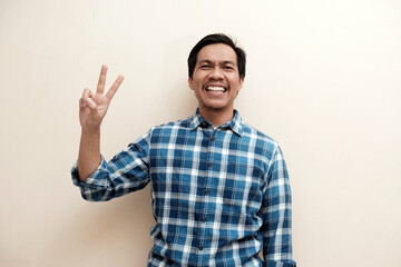 Naklejka premium Southeast Asian man wearing flannel shirt showing happy excited expression with giving number 12345 by hand gesture, on white isolated background.